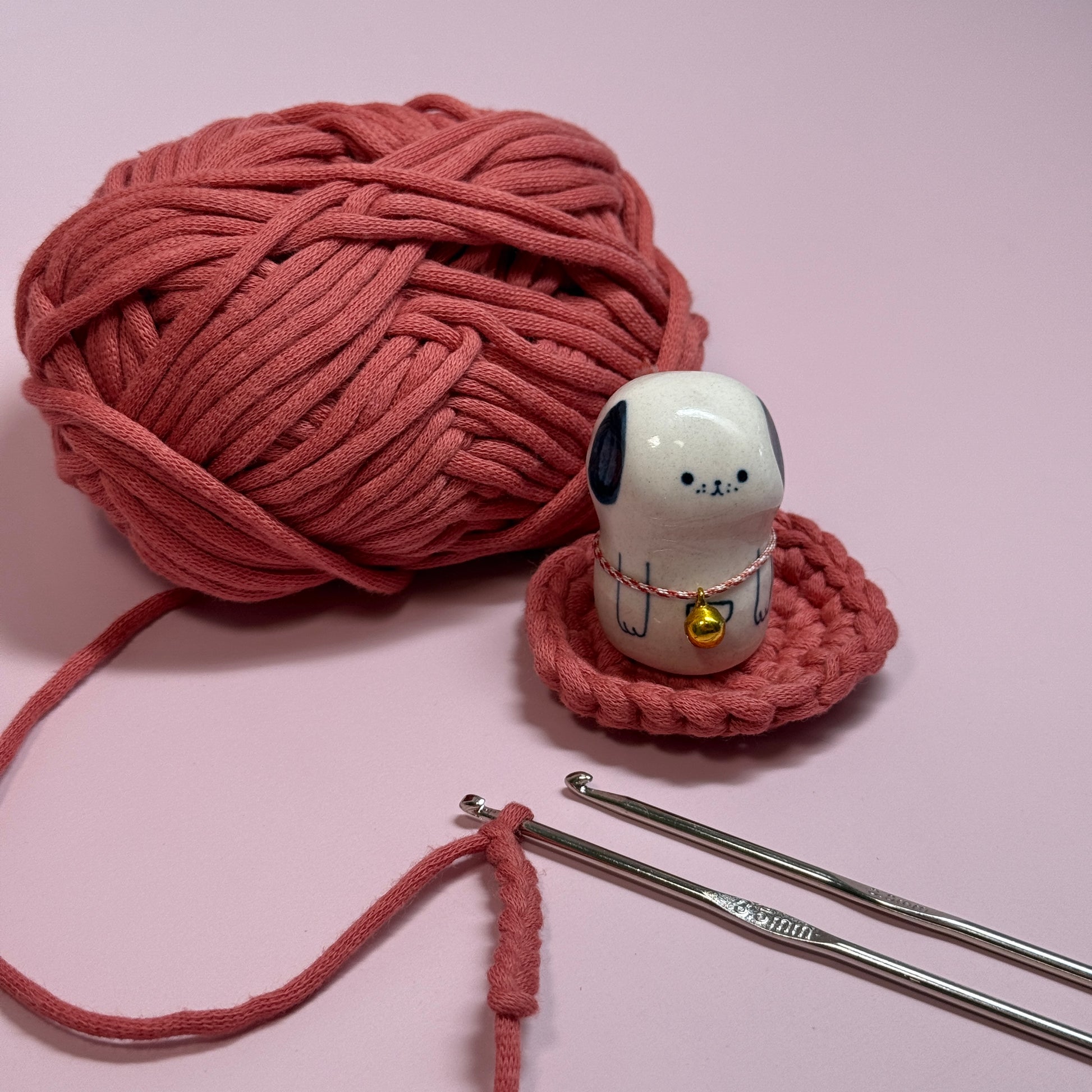 Pink yarn ball with a small decorative item and knitting needles on a pink background